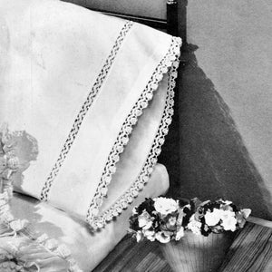 May include: A white pillow with a crocheted lace trim. The pillow is on a white bed with a floral pattern. A bouquet of white and purple flowers is in a white vase on the bed.