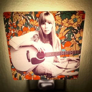 May include: A nightlight featuring a woman with long brown hair playing an acoustic guitar. The background is a colorful floral pattern.