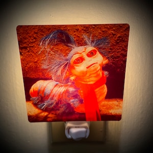 May include: A nightlight featuring a red and blue image of a creature from the movie "Labyrinth". The creature has large eyes and a furry body.