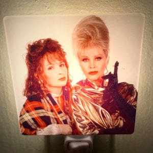 May include: A nightlight featuring a photo of two women. The woman on the left is wearing a plaid scarf and has red hair. The woman on the right is wearing a gold sequined top and has blonde hair styled in a bouffant.