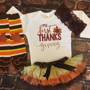 Pu&ograve; includere: Un set di abbigliamento per neonati con un body bianco a maniche lunghe con il testo "my first THANKS giving" in glitter dorato, una fascia per capelli in pizzo marrone, un gambaletto a righe marroni e arancioni con un volant marrone e una gonna di tulle a pi&ugrave; strati con un fiocco marrone.