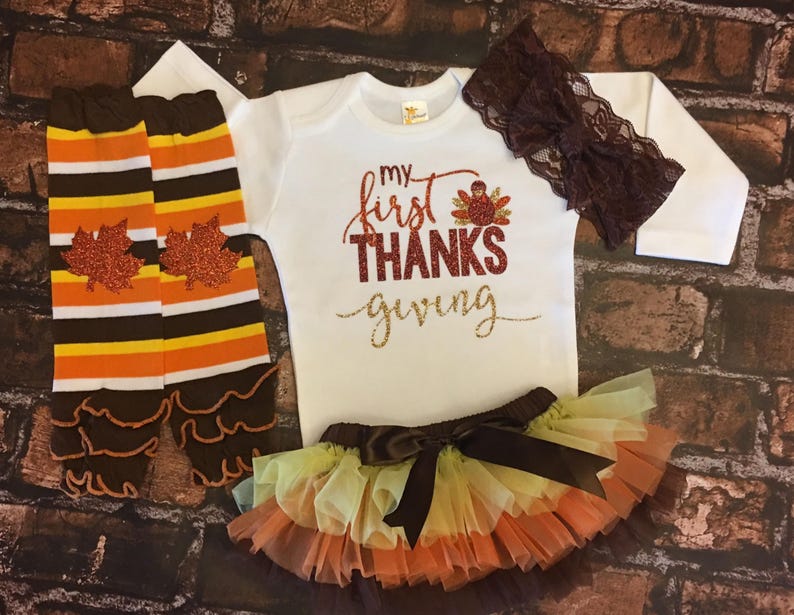Pu&ograve; includere: Un set di abbigliamento per neonati con un body bianco a maniche lunghe con il testo "my first THANKS giving" in glitter dorato, una fascia per capelli in pizzo marrone, un gambaletto a righe marroni e arancioni con un volant marrone e una gonna di tulle a pi&ugrave; strati con un fiocco marrone.