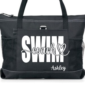 May include: Black tote bag with white text that reads "SWIM coach" with a heart symbol and the name "Ashley" below. The bag has two side mesh pockets, a zippered top, and black handles.