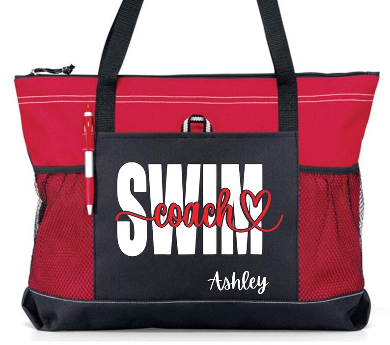 May include: Red and black tote bag with the words "SWIM coach" in white and red script, and the name "Ashley" in white script. The bag has black handles, a zippered top, and mesh side pockets. A red pen is in the side pocket.
