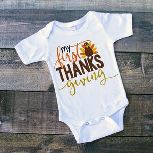 Pu&ograve; includere: Body bianco per neonato con il testo "my first THANKSgiving" e un disegno di un tacchino cartone animato.