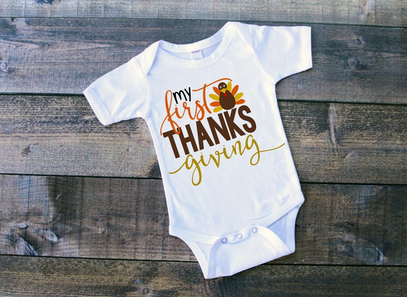 Pu&ograve; includere: Body bianco per neonato con il testo "my first THANKSgiving" e un disegno di un tacchino cartone animato.