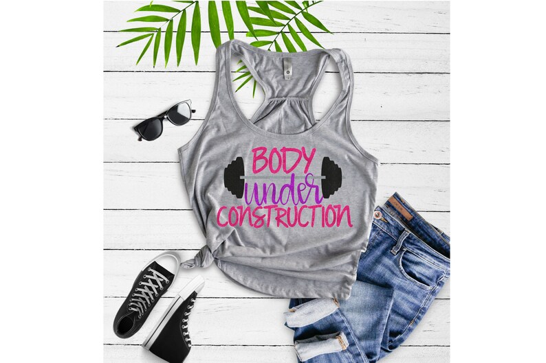 Puede incluir: Camiseta de tirantes gris con el texto "BODY under CONSTRUCTION" en letras rosa y morado con un gr&aacute;fico de mancuerna negro sobre el texto.