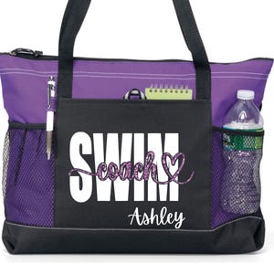 May include: A purple and black tote bag with the word "SWIM" in white block letters and "coach" in a glittery purple script. The bag has side pockets, a water bottle, and a pen. The name "Ashley" is printed below.