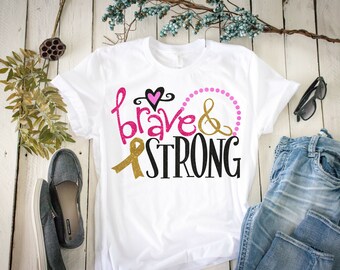 May include: White t-shirt with a pink heart, gold ribbon, and the text "brave & strong" in black lettering.