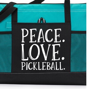 May include: A teal and black tote bag with a large front pocket that says "Peace. Love. Pickleball." in white lettering.