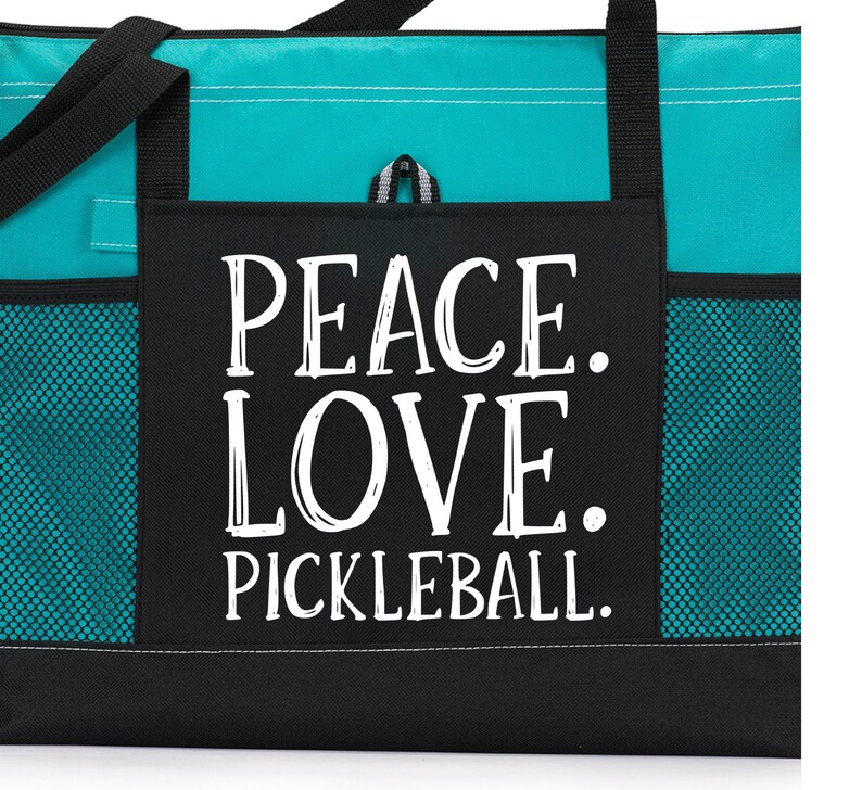 May include: A teal and black tote bag with a large front pocket that says "Peace. Love. Pickleball." in white lettering.