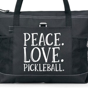 May include: Black tote bag with a large white pocket featuring the text "Peace. Love. Pickleball."