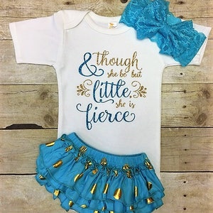 May include: A white baby onesie with gold glitter text that reads "& though she be but little, she is fierce". The onesie is paired with a blue and gold polka dot ruffle skirt and a blue lace headband.