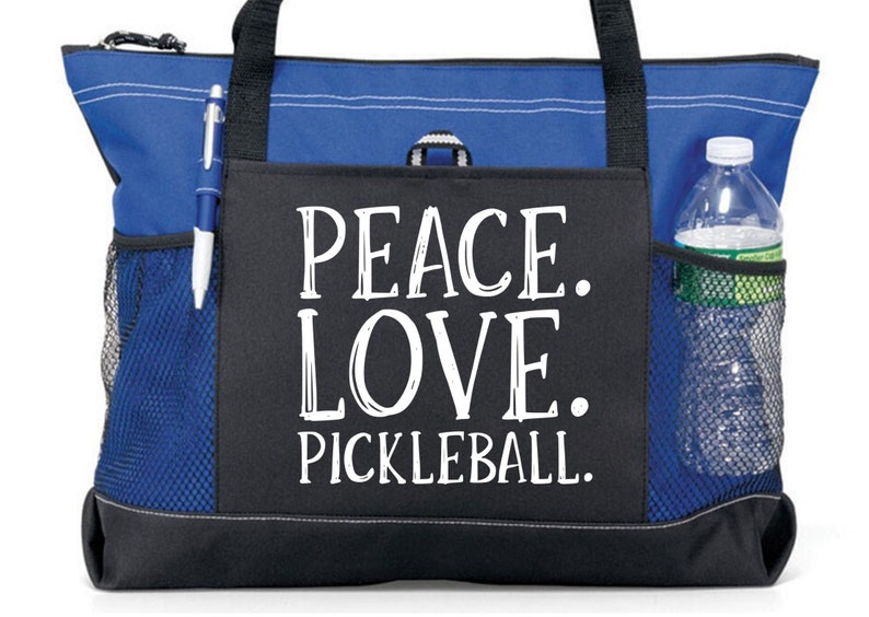 May include: A blue and black tote bag with a zippered top and mesh side pockets. The bag has a black pocket on the front with the text "Peace. Love. Pickleball." in white.