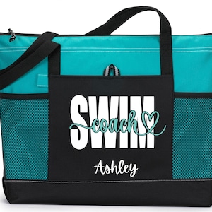 May include: A teal and black tote bag with the words "SWIM coach" and the name "Ashley" printed on the front. The bag has black handles, side pockets, and a zippered top. The bag is designed for carrying items.