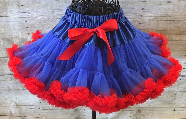 Peut inclure: Une jupe en tulle bleu avec un n&oelig;ud en satin rouge et une bordure &agrave; volants rouges.