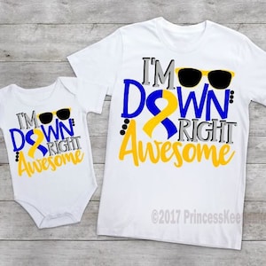 May include: Two white t-shirts with a blue and yellow ribbon design. The larger shirt says "I'm Down Right Awesome" with sunglasses. The smaller shirt says "I'm Down Right Awesome" with sunglasses.