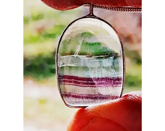 May include: A multi-colored fluorite pendant with green, white, and purple stripes. The pendant is hanging from a silver chain.