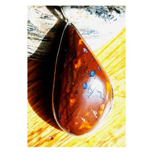 Peut inclure: Un pendentif en forme de larme avec une pierre d'opale brune et bleue. La pierre a un motif marbré avec des taches bleues.