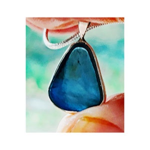 May include: A silver chain necklace with a dark blue, triangular pendant. The pendant is made of glass and has a unique, irregular shape.