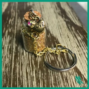 Könnte beinhalten: Schlüsselanhänger aus Glas mit goldenen Glitzer, einer goldenen Kette und einem Herz-Anhänger mit der Aufschrift "LOVE".