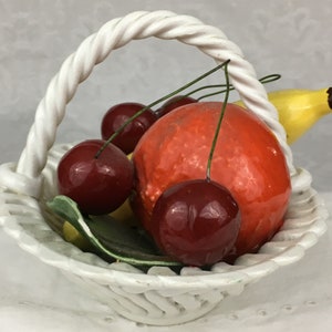 Może przedstawiać: Biały ceramiczny koszyk z uchwytem w kształcie sznura wypełniony r&oacute;żnymi owocami, w tym czerwoną pomarańczą, wiśniami i ż&oacute;łtym bananem.