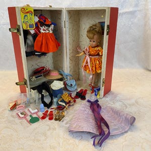 May include: A vintage doll and wardrobe set. The red and white trunk opens to reveal a doll in an orange dress, along with various miniature accessories, including hats, shoes, and dresses. The set includes a pink dress with purple ribbons.