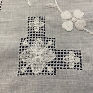 May include: White linen fabric with a delicate white embroidered design featuring a floral pattern and a grid-like pattern. The embroidery is done in a fine stitch.