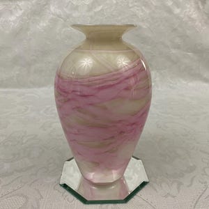 May include: A pink and white swirl glass vase with a mirrored base.