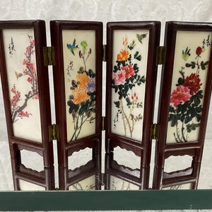 May include: A four-panel folding screen with a dark wood frame. Each panel features a painted floral design with birds. The artwork includes red, orange, and pink flowers, with green leaves and stems. The screen is a decorative home decor item.