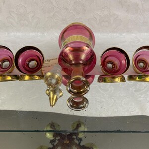 May include: A vintage glass perfume bottle set with a pink and gold design. The set includes a bottle, a stopper, and four matching atomizer tops with gold bases. The bottle and atomizer tops have a swirl pattern.