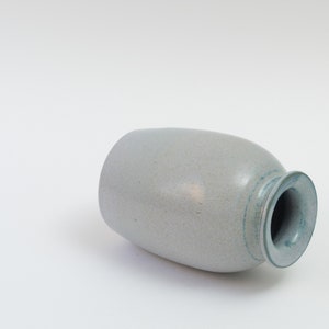Pu&ograve; includere: Un vaso in ceramica grigio chiaro con una glassa blu intorno al bordo. Il vaso ha una forma ovale e una superficie testurizzata.