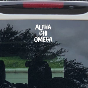 May include: A white car with a black rear window. The window has a white sticker that says "ALPHA CHI OMEGA".
