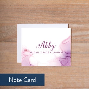 Puede incluir: Una tarjeta blanca con un fondo de acuarela p&uacute;rpura. El nombre "Abby" est&aacute; escrito en cursiva en texto p&uacute;rpura. Debajo del nombre est&aacute; el texto "Abigail Grace Fordham".