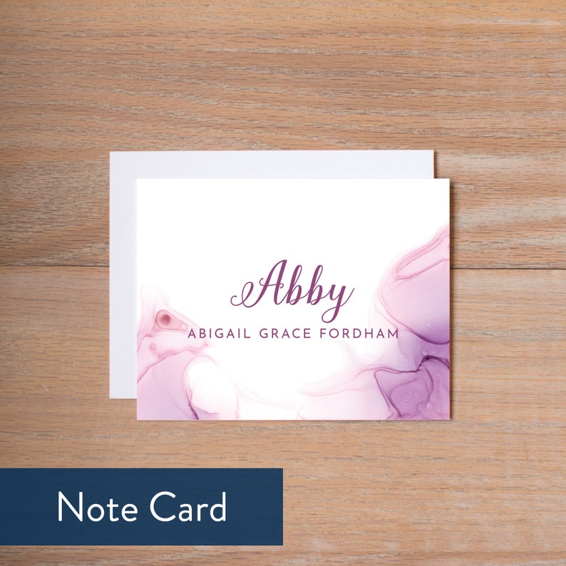 Puede incluir: Una tarjeta blanca con un fondo de acuarela p&uacute;rpura. El nombre "Abby" est&aacute; escrito en cursiva en texto p&uacute;rpura. Debajo del nombre est&aacute; el texto "Abigail Grace Fordham".