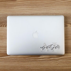 May include: A white laptop with a marble-patterned sticker that says "alpha phi" in black script.