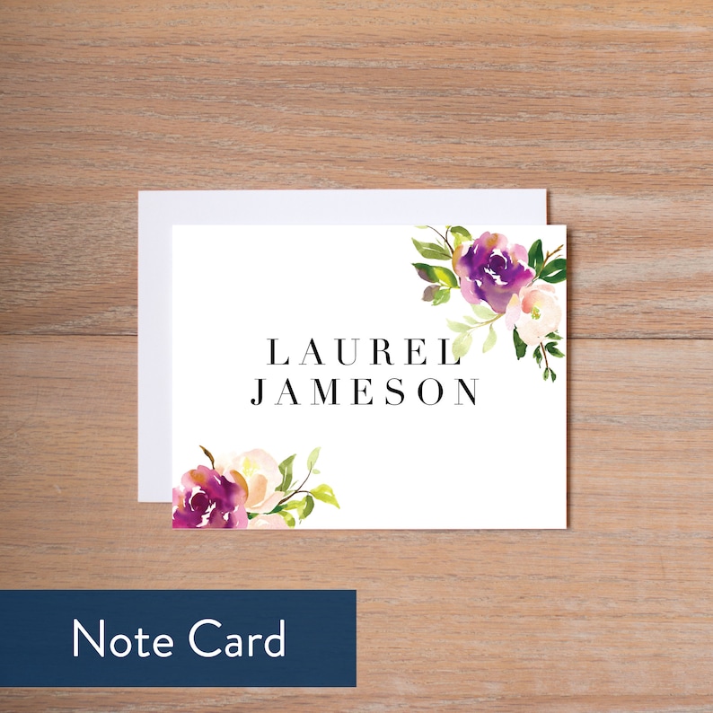 May include: A white note card with a watercolor floral design in shades of purple, pink, and green. The text "LAUREL JAMESON" is printed in black on the card. Note Card.