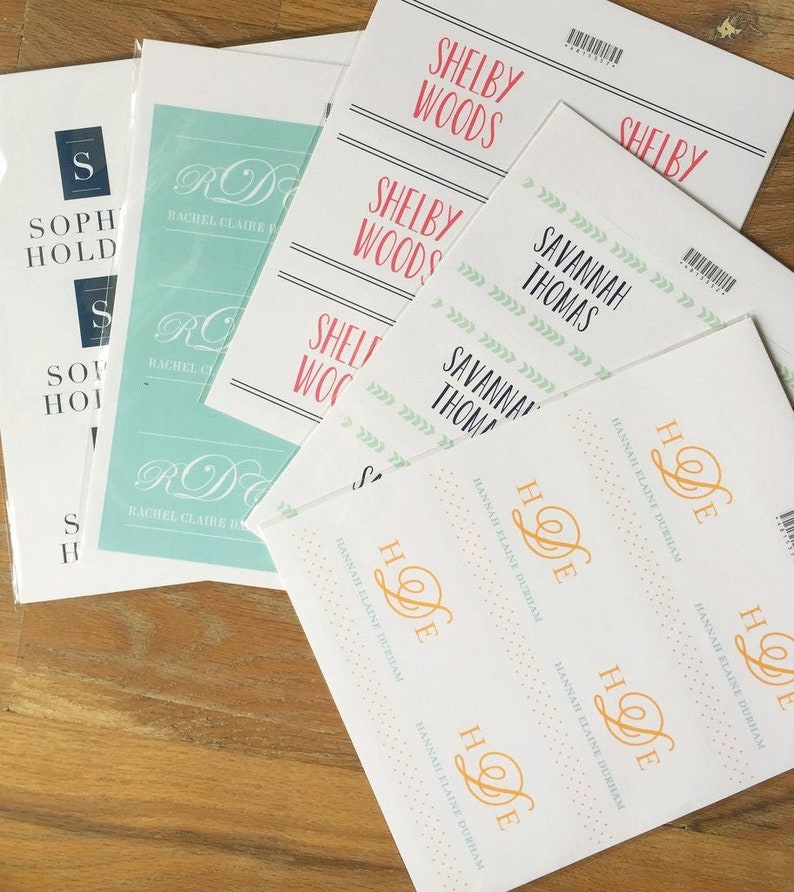 May include: A set of white cards with various names printed on them. The names include Shelby Woods, Savannah Thomas, Rachel Claire, and Hannah Elaine Durham. The cards are decorated with different patterns, including green leaves, gold glitter, and a light blue background.
