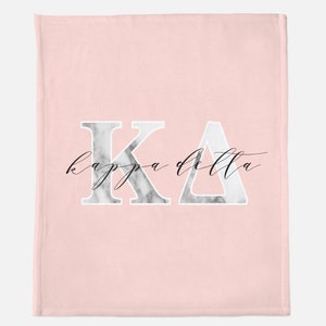 May include: Pink fleece blanket with a white marble design featuring the letters "KA" and the text "kappa delta" in black cursive.