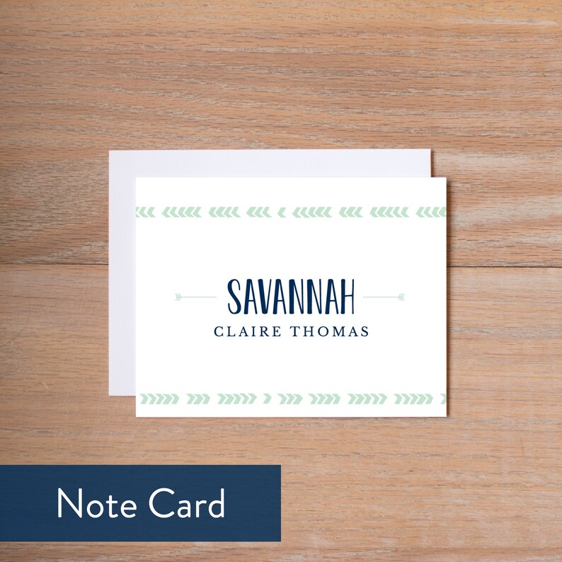 May include: A white note card with the name "SAVANNAH" in navy blue, and "CLAIRE THOMAS" below it. The card has a light green arrow design along the top and bottom edges. A white envelope is behind the card. The words "Note Card" are in a navy blue box.
