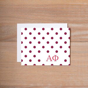May include: White card with a red polka dot pattern and the letters "AΦ" in pink.