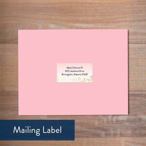 May include: A pink mailing label with a gold and white patterned border. The text on the label reads "Alpha Omicron Pi, 800 Lakeshore Drive, Birmingham, Alabama 35229".