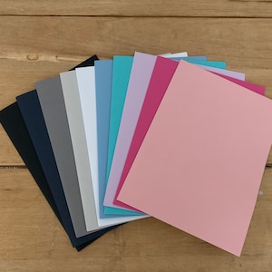 May include: A fan of 10 different colored sheets of paper. The colors are black, navy blue, gray, white, light blue, teal, lavender, pink, and light pink.
