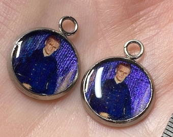 May include: Two silver charm pendants with a blue and purple background and a picture of a person wearing a blue jacket.