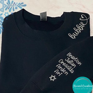 May include: Black sweatshirt with white embroidery. The embroidery includes the word "bubbie" with a heart, a Star of David, and a list of names: Braxton, Julian, Cressida, Arden, Ari.