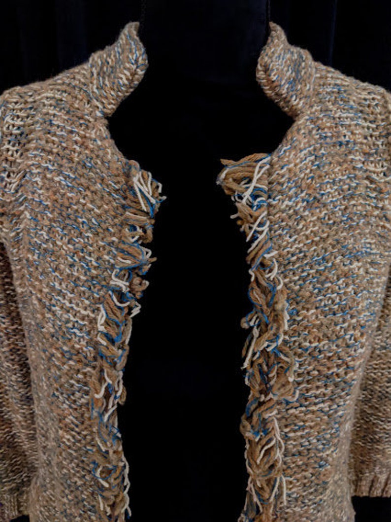 May include: A brown and blue knitted cardigan with fringe detailing on the edges.