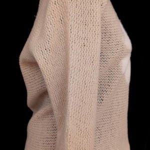 May include: A light beige, open-knit sweater with long sleeves. The sweater has a loose, relaxed fit and a slightly textured appearance. The image is set against a black background, highlighting the sweater's color and texture.