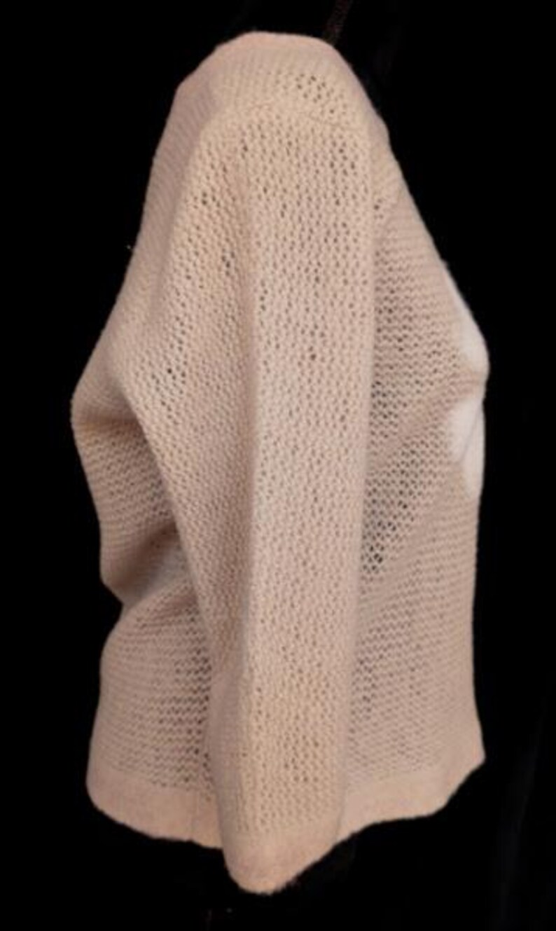 May include: A light beige, open-knit sweater with long sleeves. The sweater has a loose, relaxed fit and a slightly textured appearance. The image is set against a black background, highlighting the sweater's color and texture.
