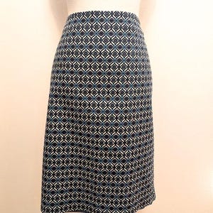 K&ouml;nnte beinhalten: Ein knielanger Rock mit einem geometrischen Muster in Marineblau, Wei&szlig; und T&uuml;rkis. Der Rock hat eine taillierte Taille und eine leichte A-Linien-Form. Der Stoff scheint ein gewebtes Material zu sein.