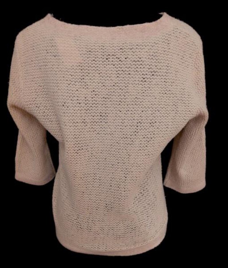 May include: A light pink, open-knit sweater with a boat neck and three-quarter sleeves. The sweater has a relaxed fit and a slightly textured appearance. The sleeves are wide and taper towards the elbow.